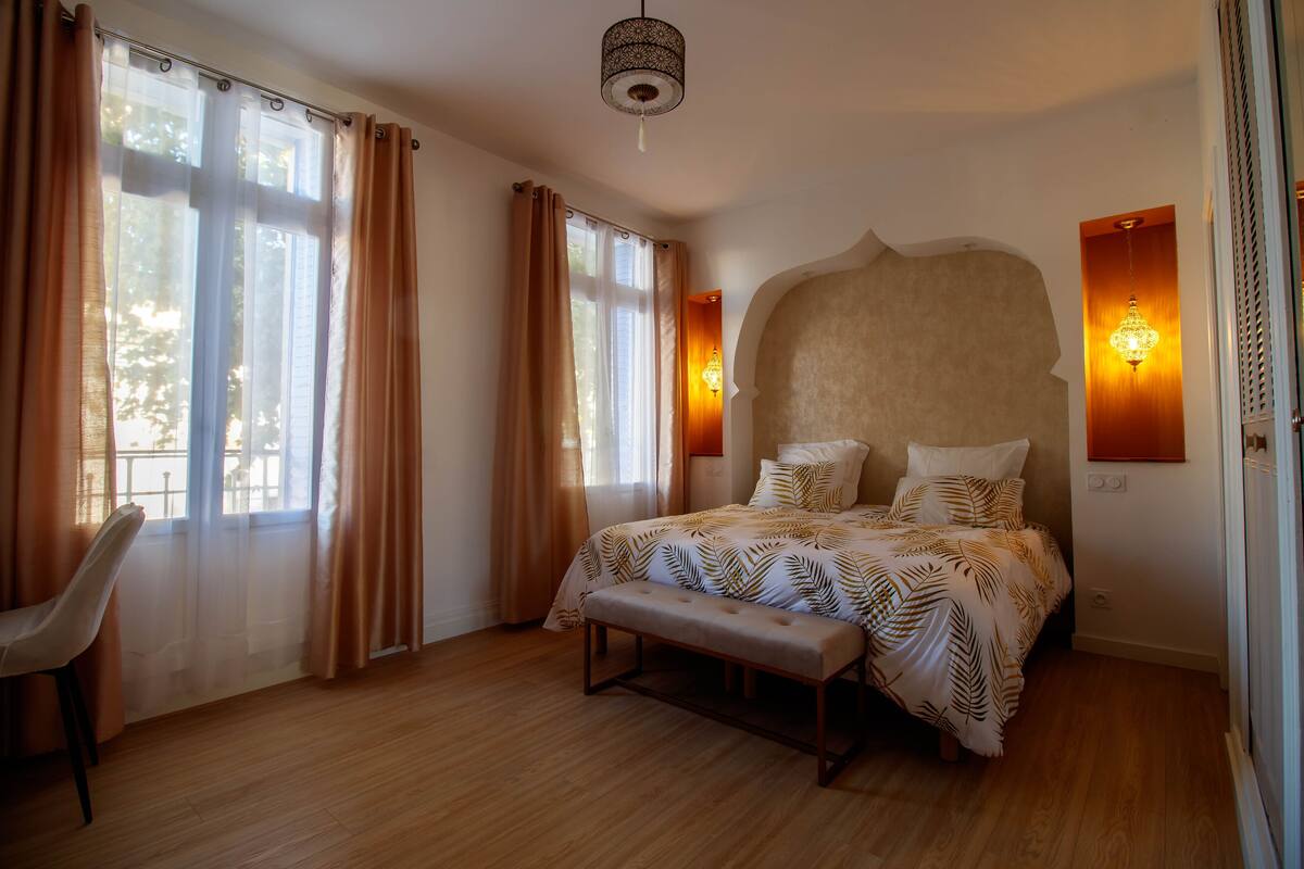 Un dormitorio con cama, banca, silla y dos apliques de pared.
