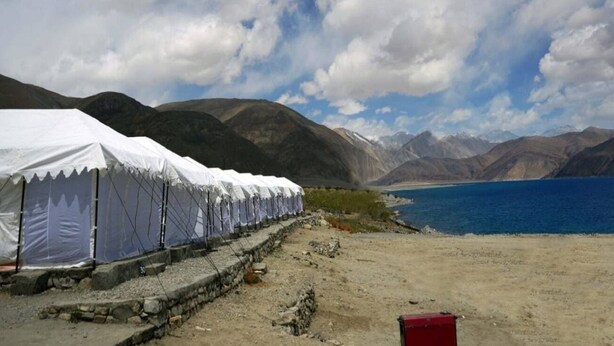 A row of white tents along a stone wall by a lake with mountains in the background. - Martsemik Camping Spangmik (Leh)