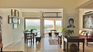 A spacious living area with a dining set, a sofa, and a view of a cityscape through large windows. - Stunning Art filled / Water View apt in Kochi (Ernakulam)