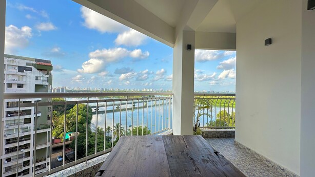 A balcony with a view of a river, buildings, and a clear sky. - Stunning Art filled / Water View apt in Kochi (Ernakulam)