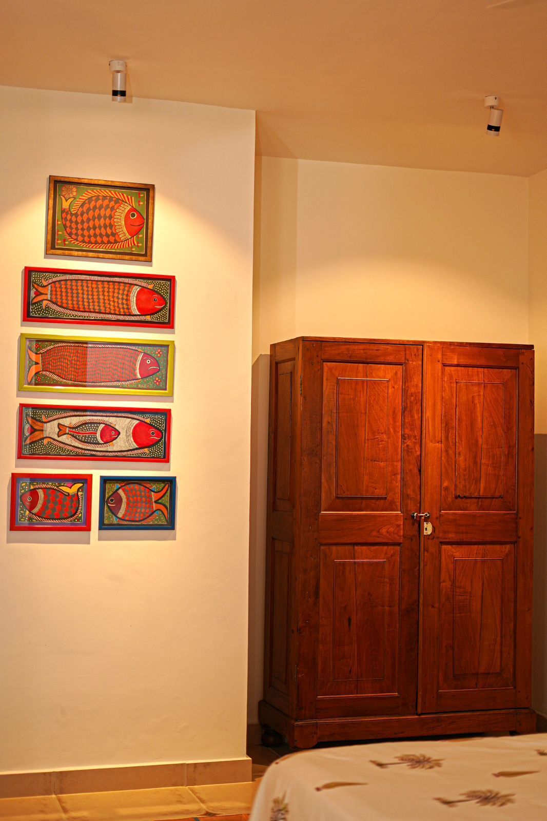 Un dormitorio con un armario de madera, una cama con colcha estampada y cuatro cuadros enmarcados con pinturas de peces en la pared.