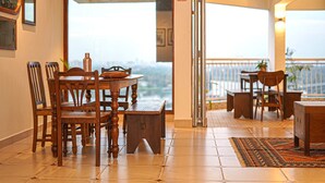 A dining area with a wooden table and chairs, a small cabinet, and a view of the city through a glass door.