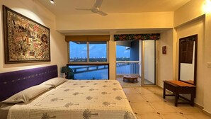 A bedroom with a bed, a ceiling fan, a large window, a balcony, and a painting on the wall. - Stunning Art filled / Water View apt in Kochi (Ernakulam)