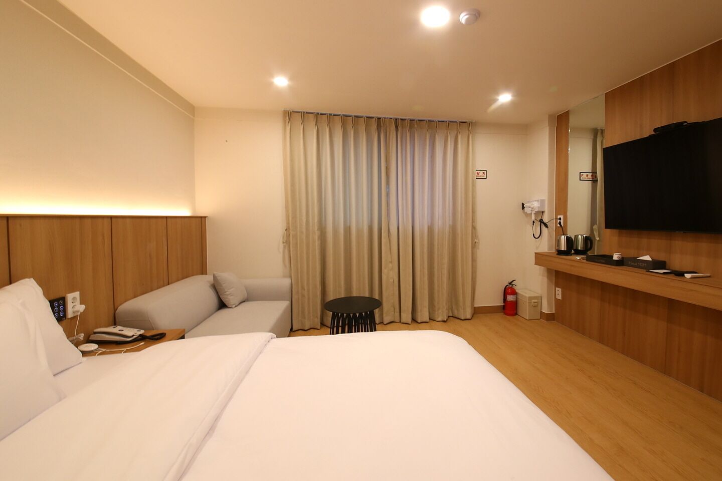 A hotel room with a large bed, a sofa, a small table, a TV, and a mirror.