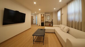A modern living room with a flat-screen TV, a sofa, a coffee table, and a small desk with a mirror. - MGM Hotel (Gangneung)