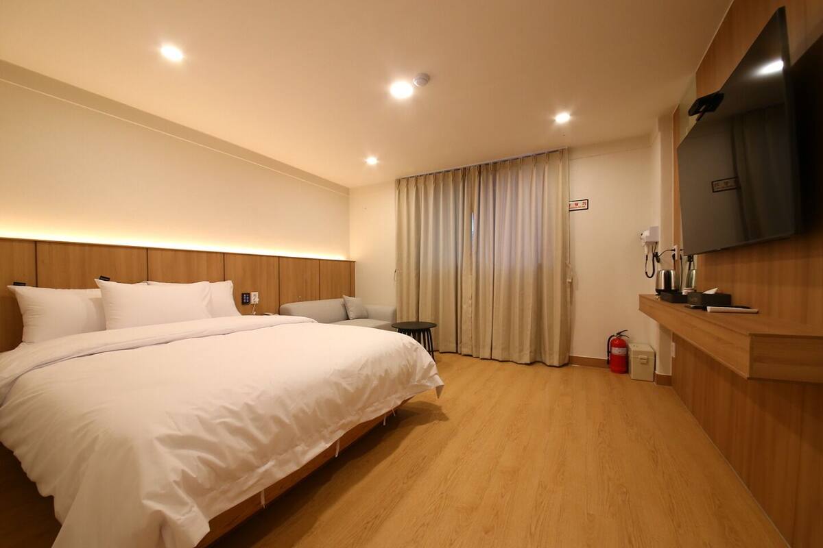 A hotel room with a large bed, a small table, a TV, and a fire extinguisher.