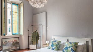 A bedroom with a bed, a window, a radiator, a coat rack, and a painting.