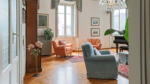 A spacious living room with a grand piano, a chandelier, and a large window with a view.