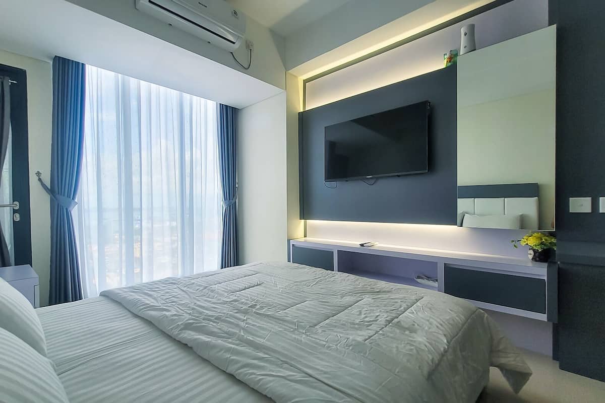 Ein modernes Hotelzimmer mit einem großen Bett, einem flachbildfernseher an der Wand und einem Fenster mit Vorhängen.