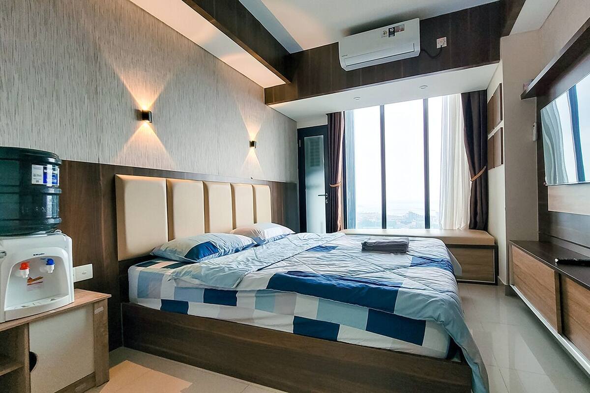 Ein modernes Hotelzimmer mit einem großen Bett, einem Wasserspender, einem Fernseher und einem Fenster mit Vorhängen.