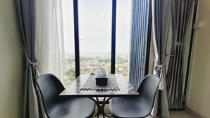 Quarto com uma mesa, duas cadeiras, uma janela com vista para a cidade e cortinas de ambos os lados da janela.