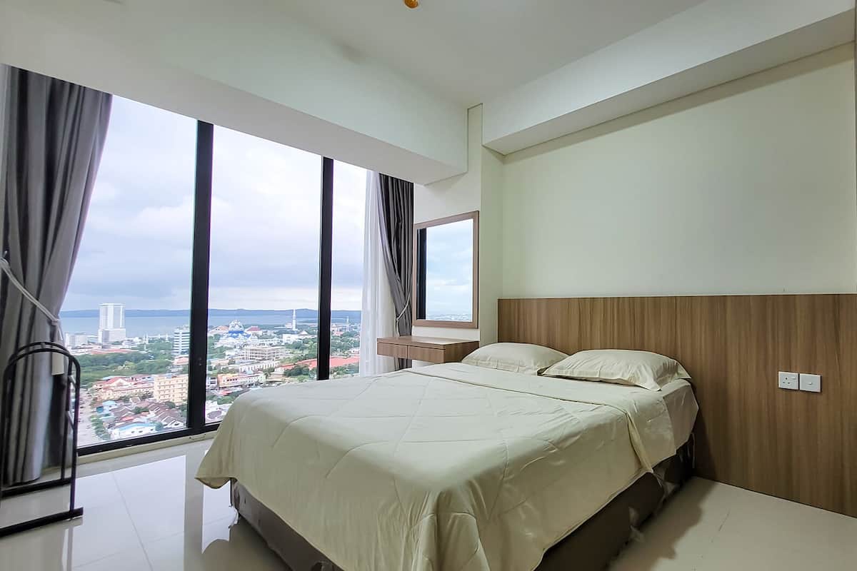 Ein modernes Schlafzimmer mit einem großen Bett, einem Holzkopfteil und Blick auf eine Stadtlandschaft durch große Fenster.