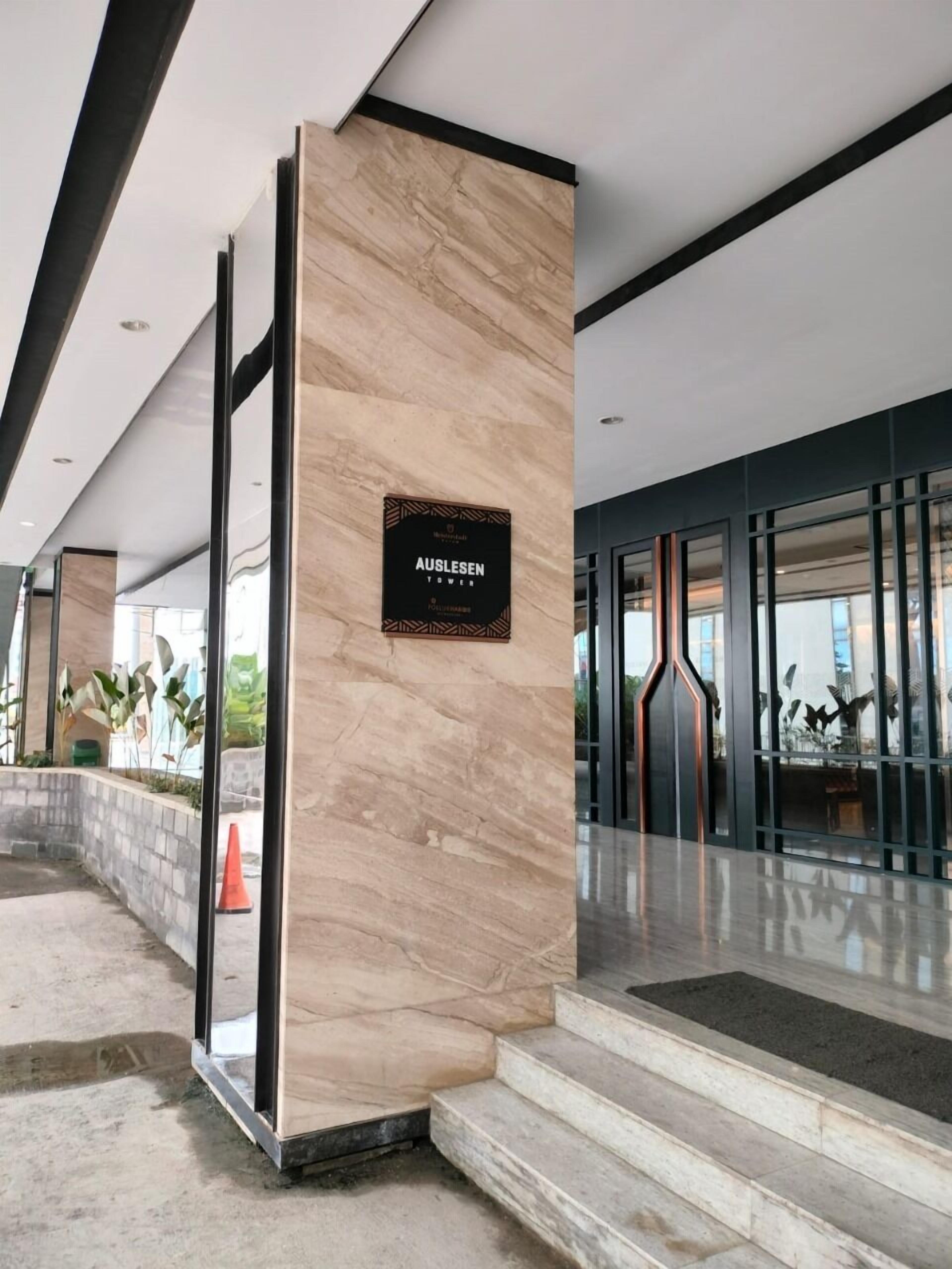 A modern building entrance with a marble column, a sign reading "AUSLESEN TOWER," and a glass door leading inside.