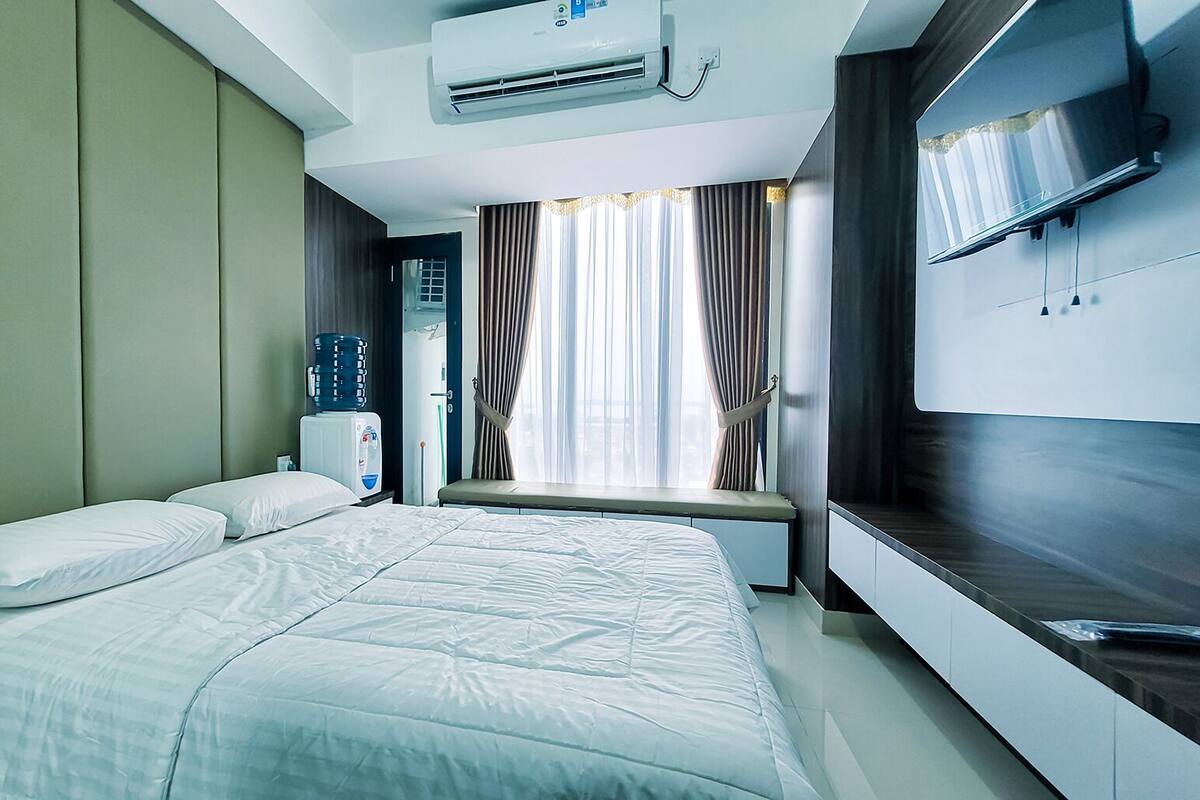 Ein modernes Hotelzimmer mit einem großen Bett, einem integrierten Fernseher und einem Fenster mit Vorhängen.