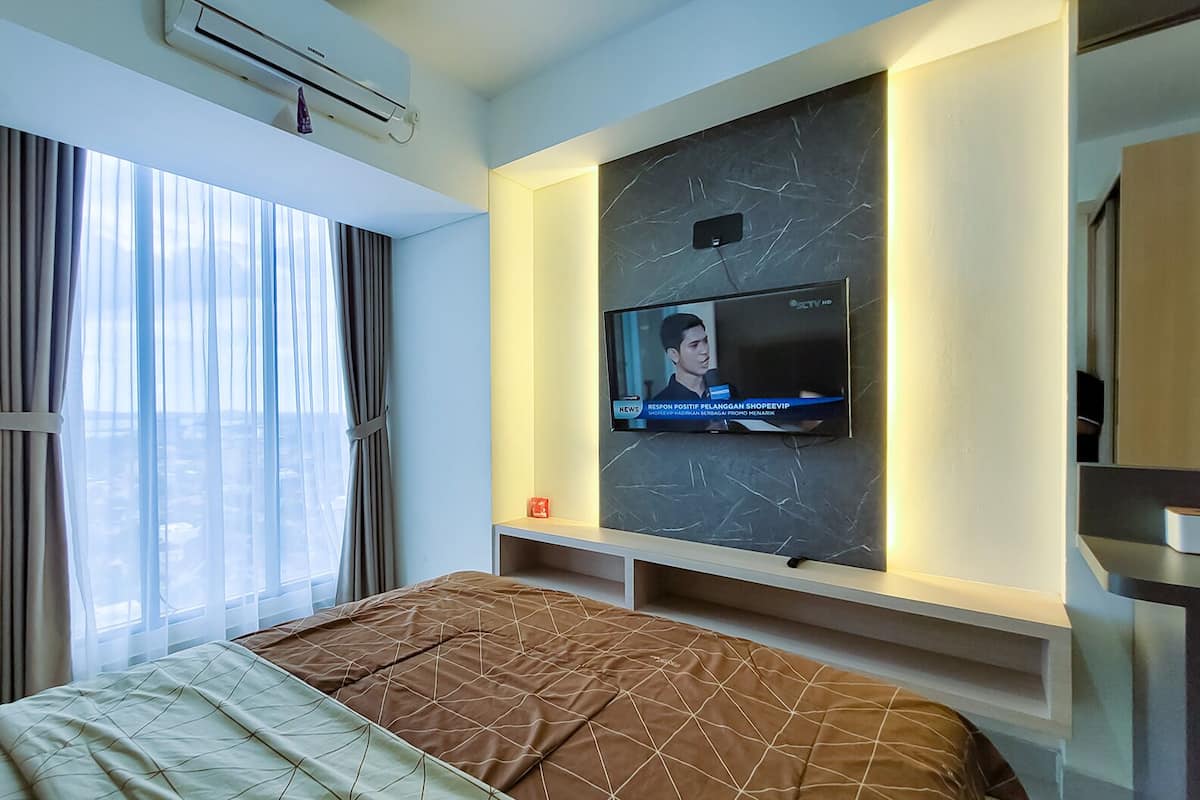 Ein Hotelzimmer mit einem Bett, einem an der Wand montierten Fernseher und einem Fenster mit Vorhängen.