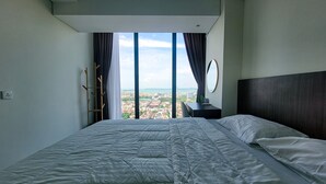 Quarto moderno com uma cama grande, mesa de cabeceira, espelho e vista para a cidade através de amplas janelas.