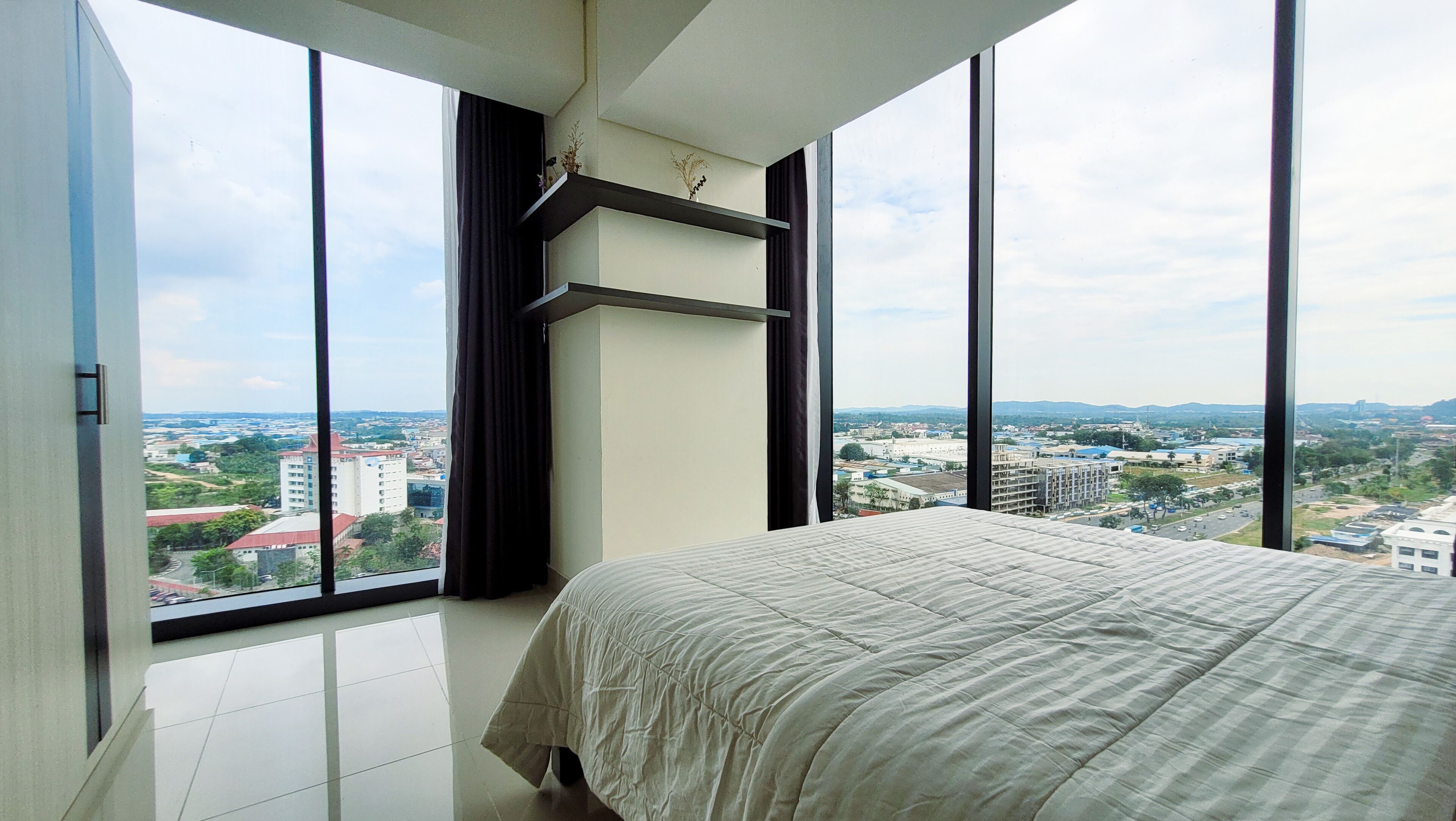 A bedroom with a large bed, a view of a cityscape through floor-to-ceiling windows, and a modern interior design.