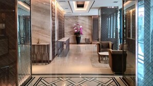 Um hall moderno com um padrão geométrico no chão, um balcão de recepção, área de estar e um arranjo floral decorativo.