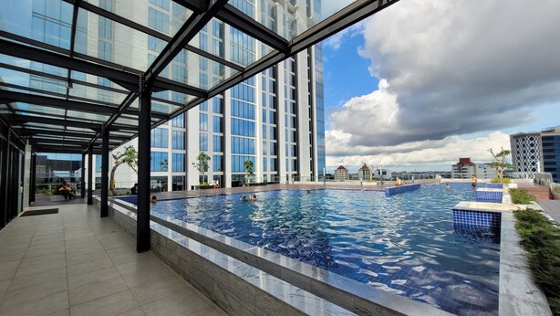 Piscina no terraço com guarda-corpo de vidro e vista para edifícios ao redor.