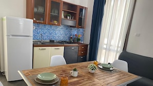 Cocina compacta con refrigerador, estufa y alacenas. Hay una mesa de comedor con sillas y una pequeña planta en maceta.