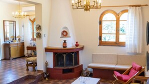 A spacious living room with a fireplace, a large window, and a cozy seating area. - All Seasons Guest House (Lake Plastiras)