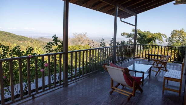 A covered outdoor seating area with a table and chairs, overlooking a scenic landscape. - All Seasons Guest House (Lake Plastiras)