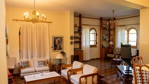 A spacious living room with a chandelier, a television, and a bookshelf. - All Seasons Guest House (Lake Plastiras)