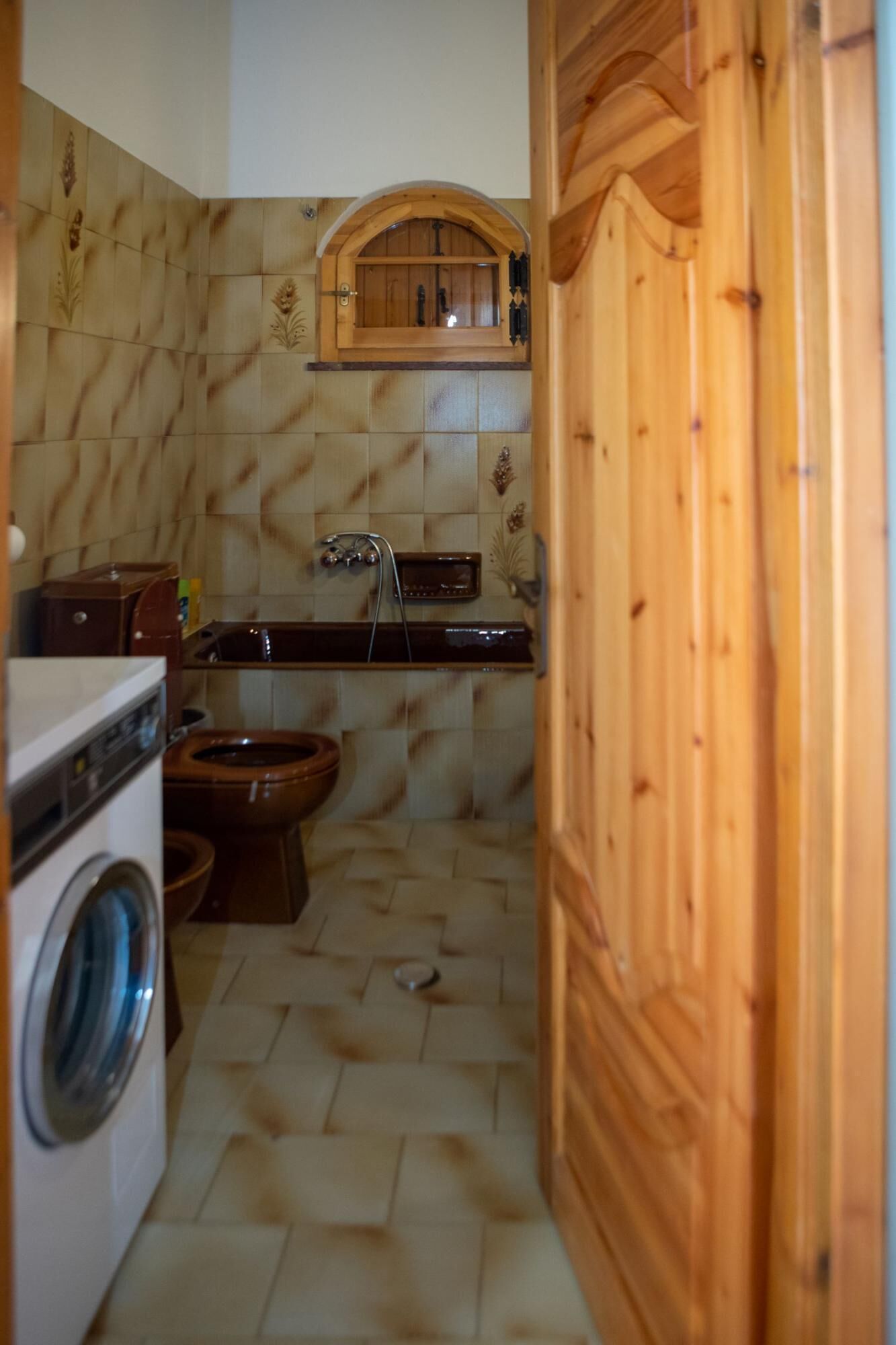 A compact kitchen with a washing machine, a wooden cabinet, and a tiled backsplash.