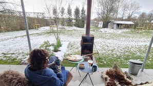 Una persona sentada en una silla con un libro, una taza y un plato de comida sobre una mesa en un área exterior nevada con un hogar a leña.