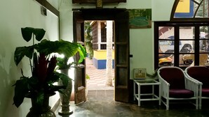 A hallway with a large plant, a reception desk, and two chairs. - Falcon Resorts by Dia Hotels (Calangute)