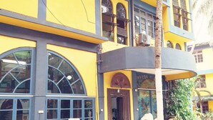 A multi-story building with yellow and blue exterior walls, large arched windows, and a checkered tile floor. - Falcon Resorts by Dia Hotels (Calangute)