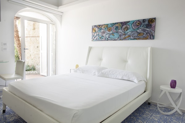 Une chambre avec un grand lit, une chaise, une petite table et un tableau abstrait aux couleurs vives accroché au mur.
