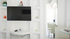 Una sala moderna con un televisor de pantalla plana montado en una pared blanca, una mesa de centro de vidrio y un sofá blanco.