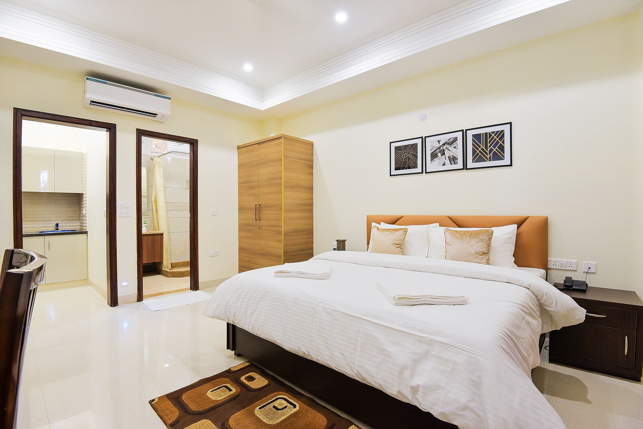 A modern hotel room with a large bed, a wardrobe, a bathroom with a mirror, and a small bedside table.