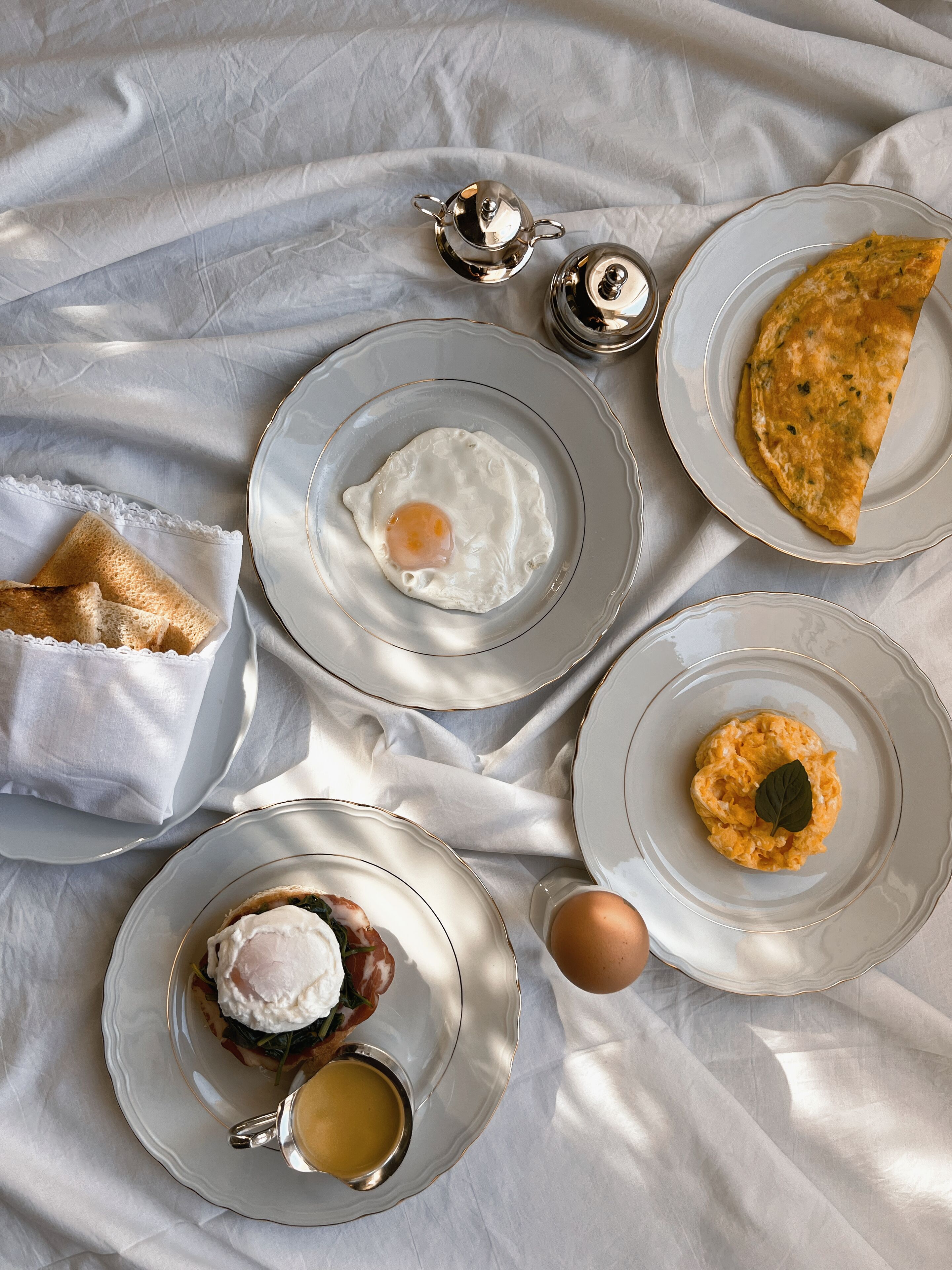 A breakfast setting with various dishes including eggs, toast, and a rolled omelette on a table with a white tablecloth.