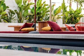 A poolside area with lounge chairs and cushions, surrounded by lush green plants. - Palazzo Piccinno (Parabita)