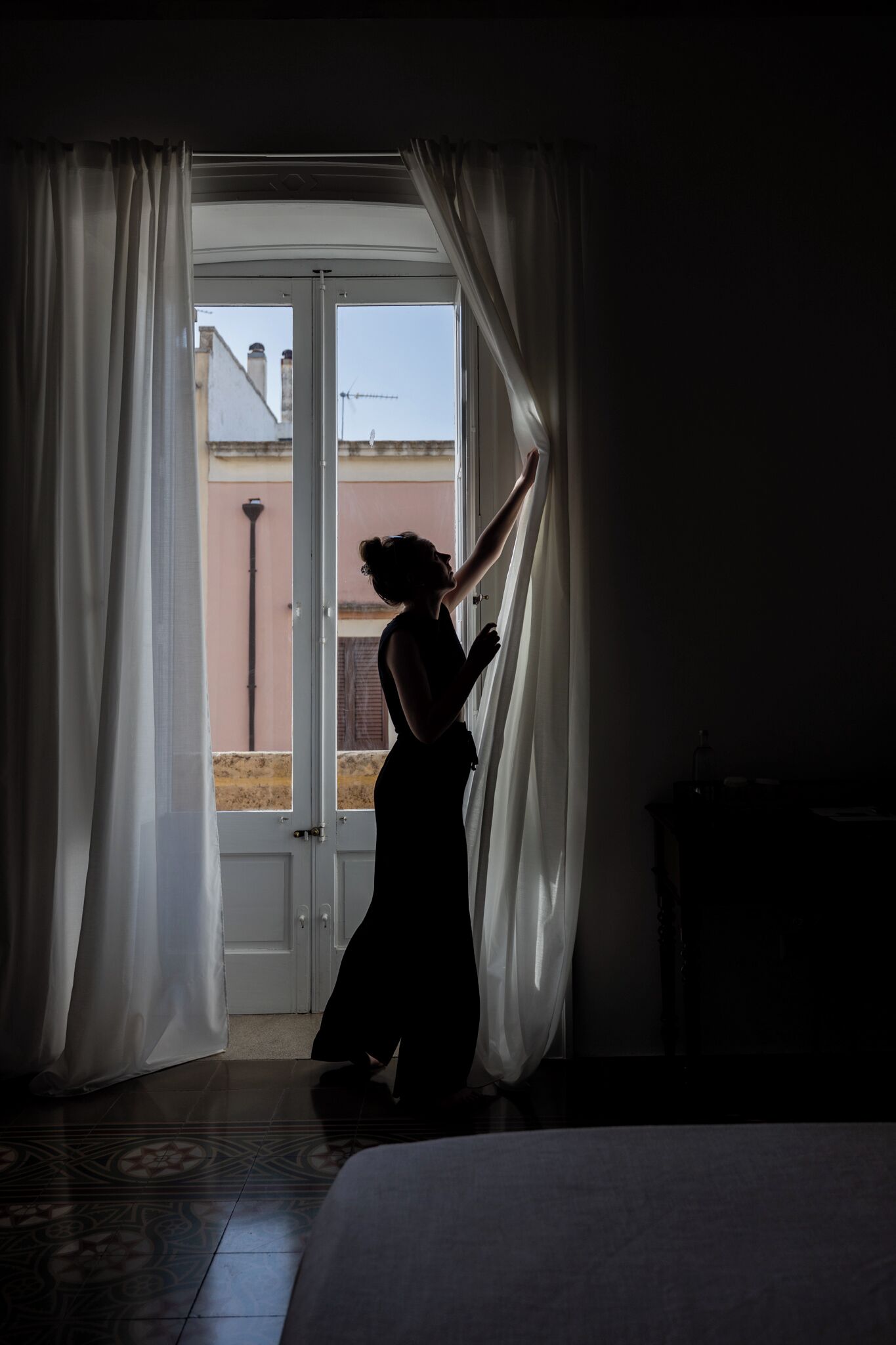 Una habitación con cama, ventana con cortinas y vista a edificios.