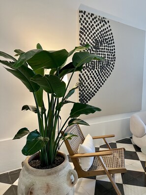 Relax in a stylish space with a woven chair, a large potted plant, and a unique wall art piece.