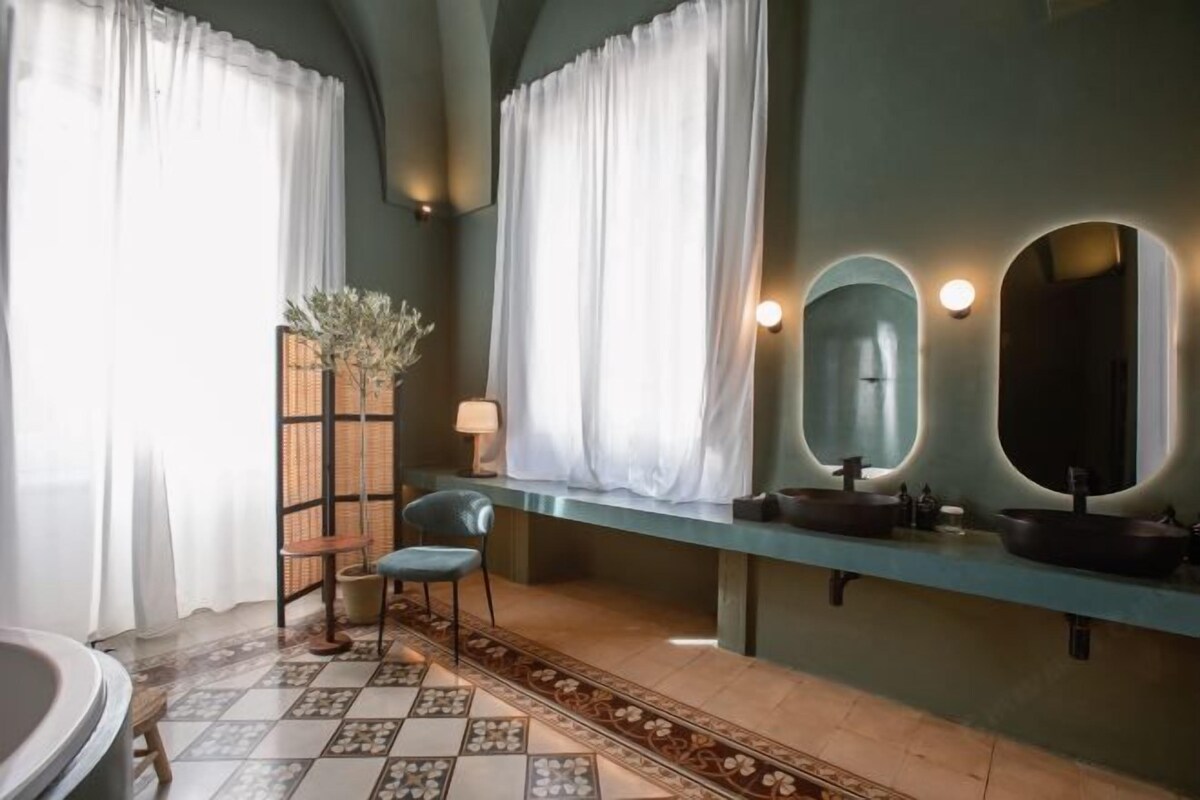 Une salle de bain avec un grand miroir, deux lavabos, une chaise et une plante décorative.