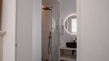 A modern bathroom with a glass-enclosed shower, a white sink with a black basin, and a mirror with a circular light.