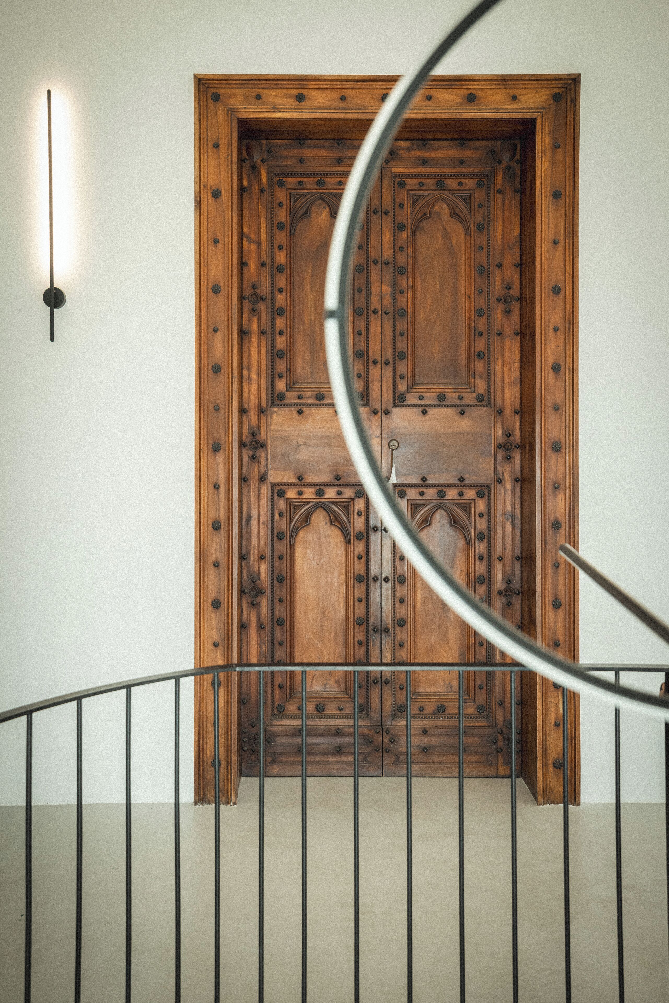 Una puerta de madera con detalles metálicos intrincados, una lámpara en la pared y una barandilla metálica al frente.