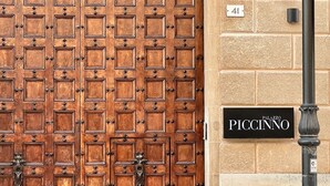 Suuri puinen ovi, jossa on ruudukkomainen kuvio, ja sen molemmin puolin kivimuuri sekä katukyltti, jossa lukee ”Palazzo Piccino”.