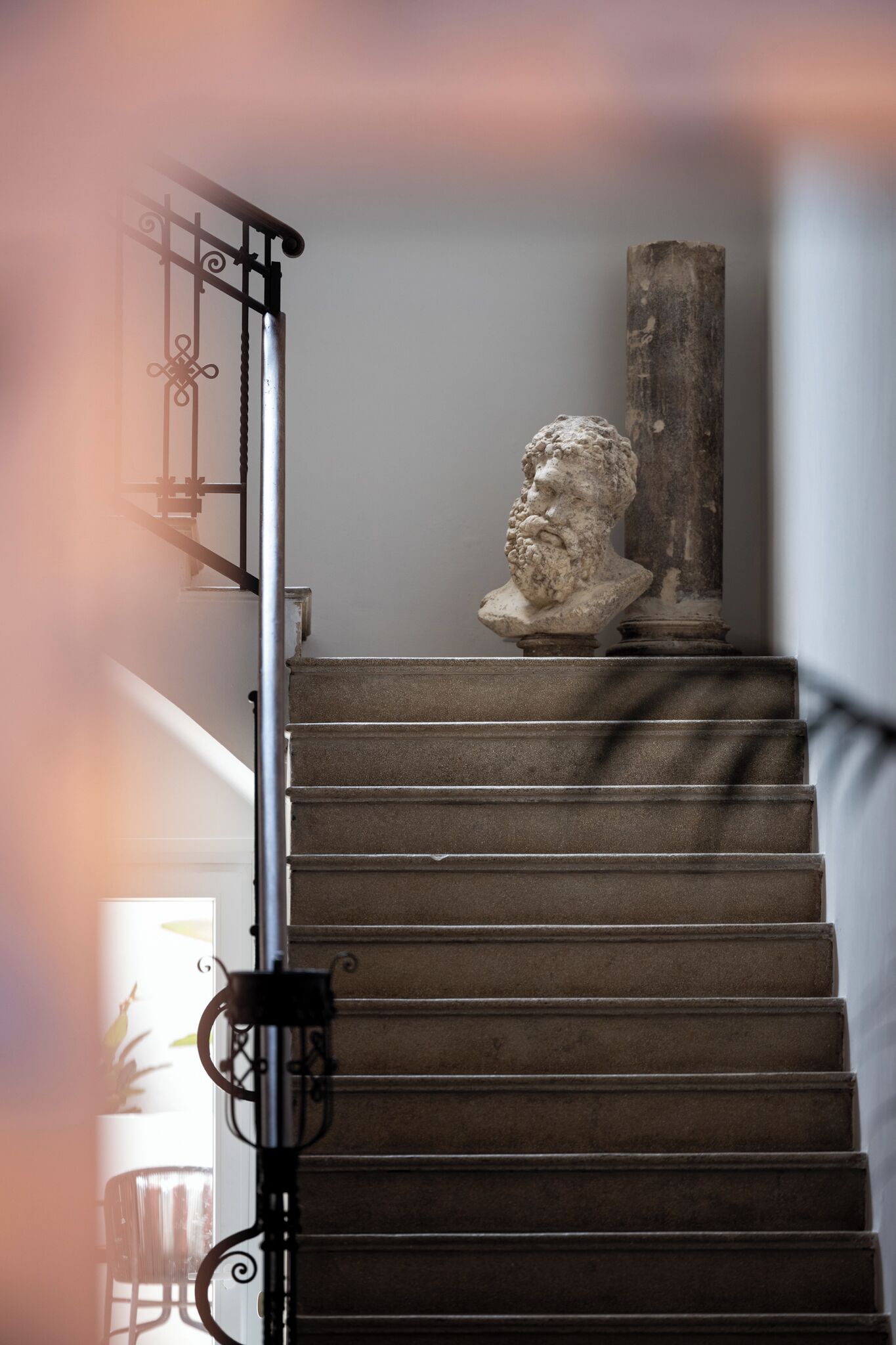 A staircase with a stone balustrade and a classical bust sculpture on the landing.