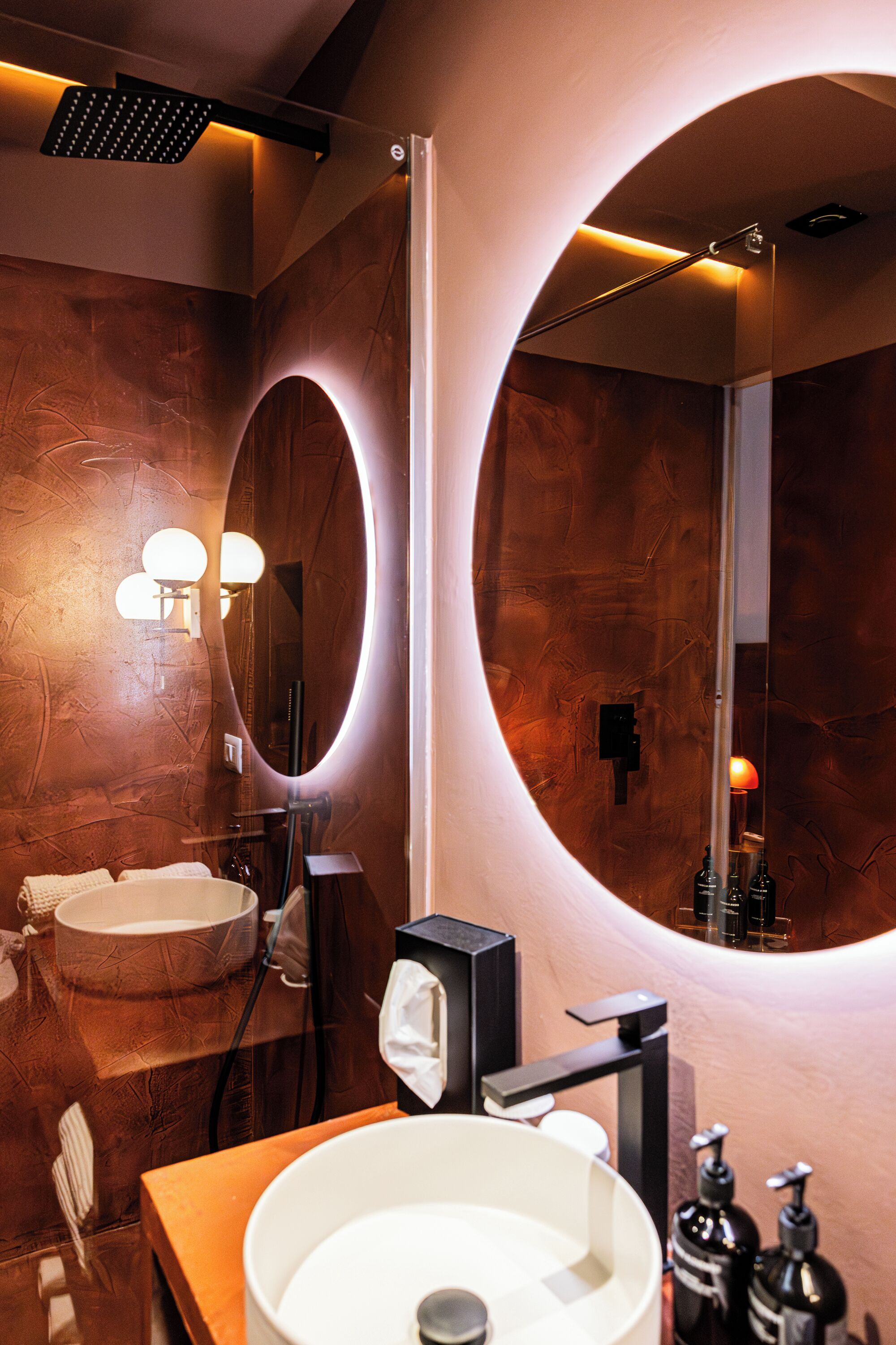 A modern bathroom with a large oval mirror, a round sink, and a towel rack.