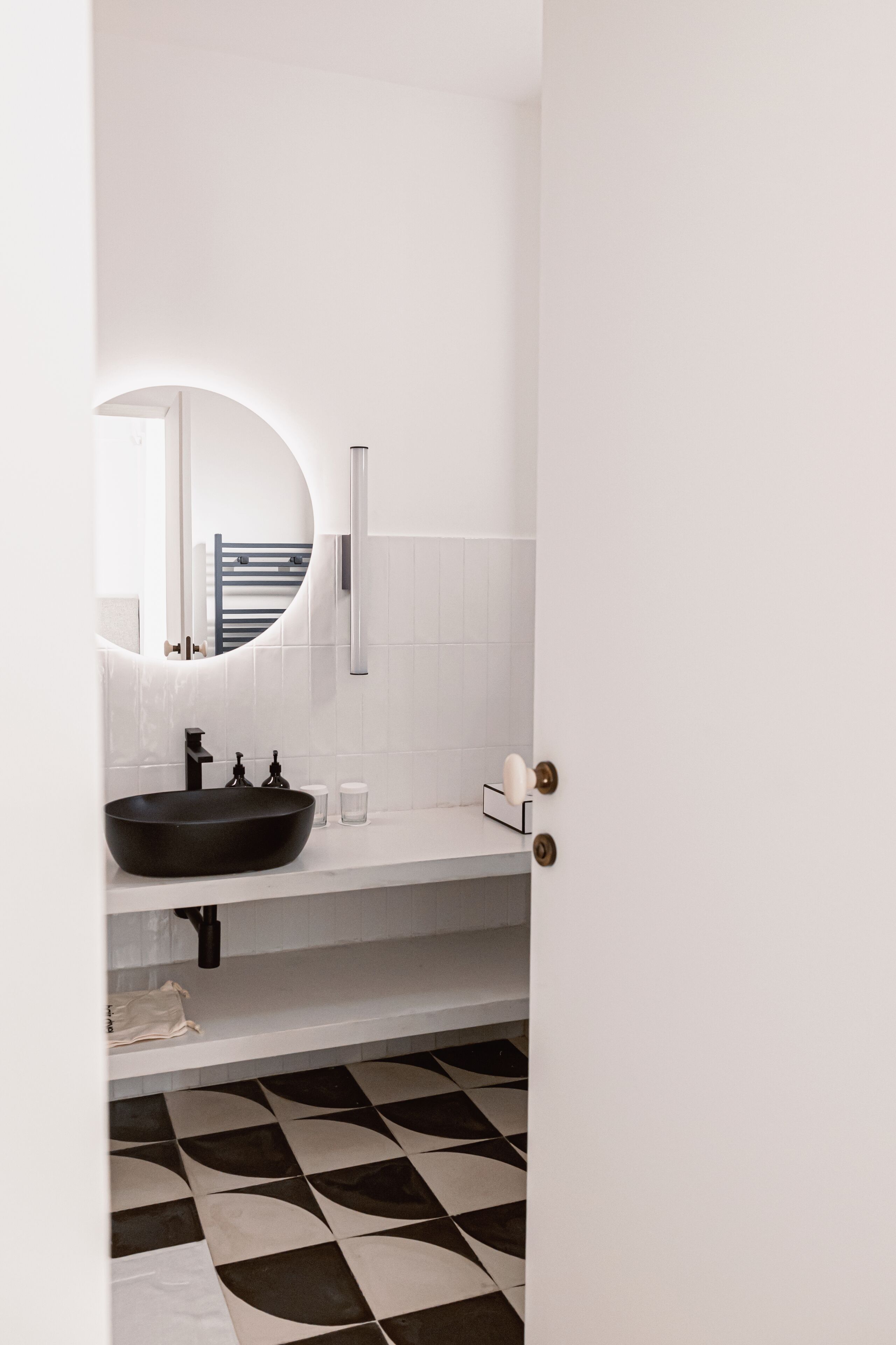 Een badkamer met een zwart wastafel, witte tegels, een ronde spiegel en een geruite vloer.