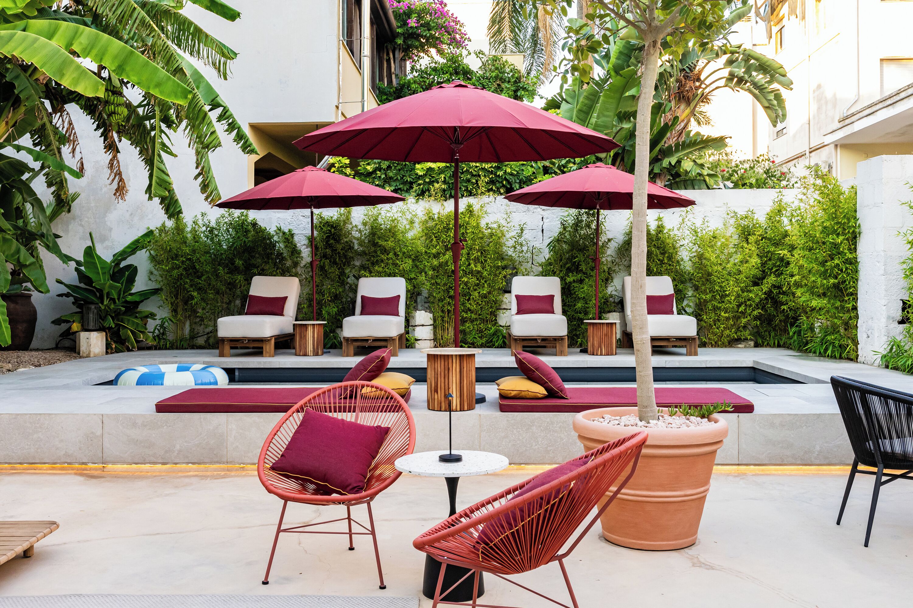 An outdoor seating area with wicker chairs, red cushions, and large umbrellas.