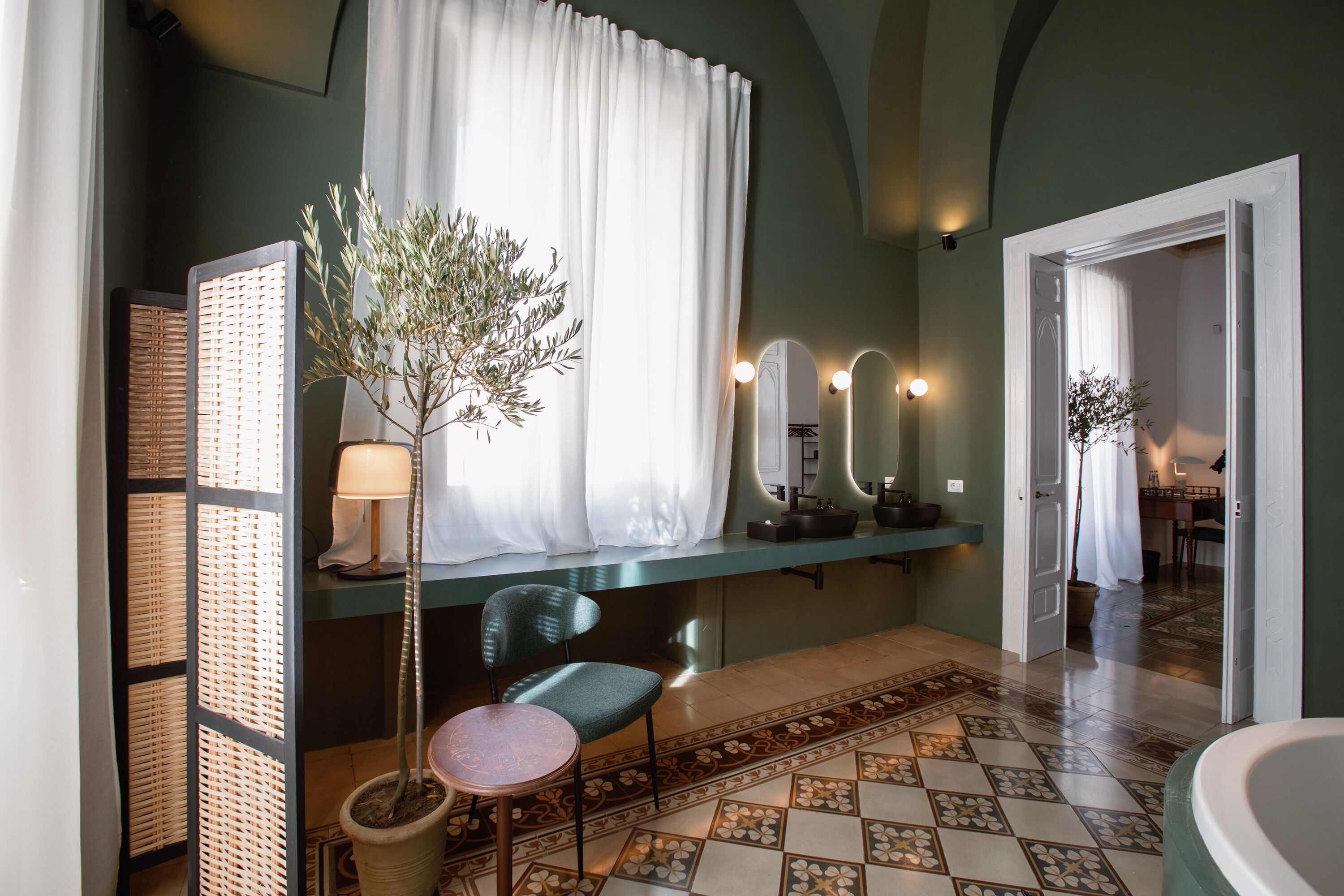 Une salle de bain avec une baignoire, un lavabo, une chaise, une plante en pot et un miroir avec éclairage.