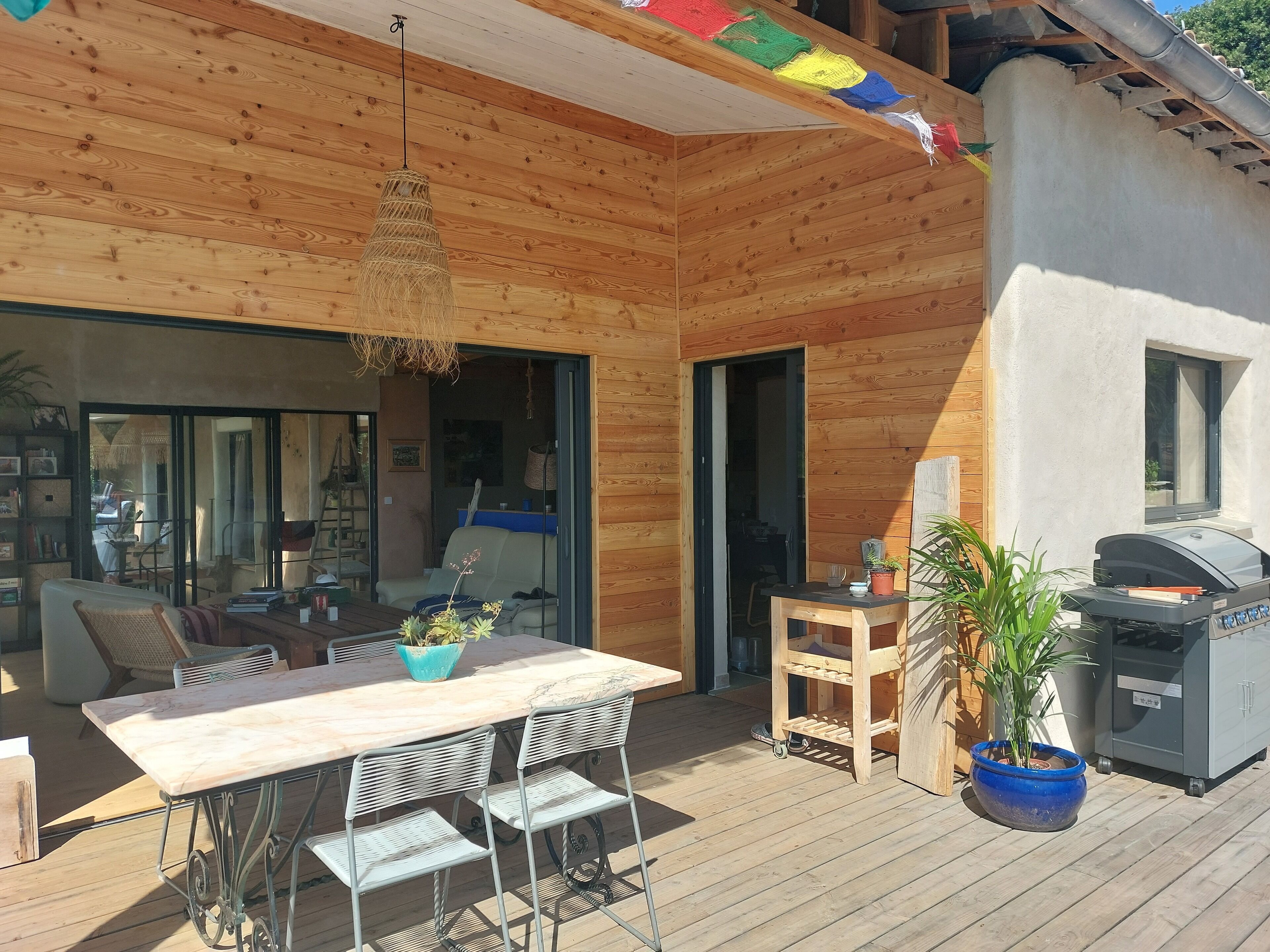 A wooden deck with a dining table and chairs, a hanging light fixture, and a barbecue grill.