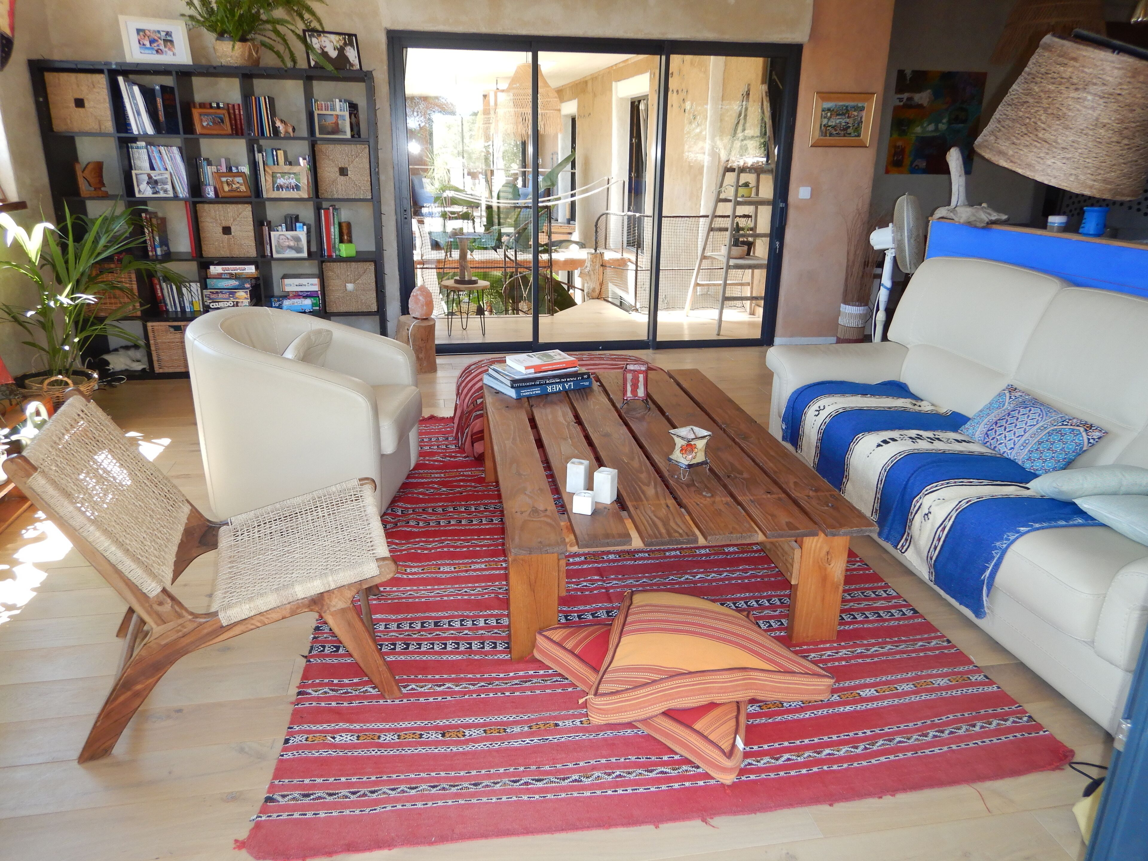 A living room with a sofa, chairs, a coffee table, a bookshelf, and a view through a glass door to an outdoor area.