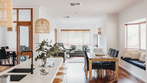 A modern living room with a dining area, a sofa, and a large window with blinds. - Skillogalee Estate (Spring Gully)